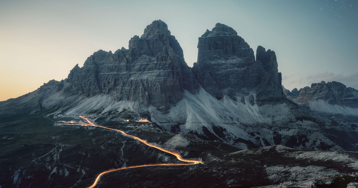 The Tre Cime di Lavaredo peaks in the Italian Dolomites at dusk, with light trails on the road below