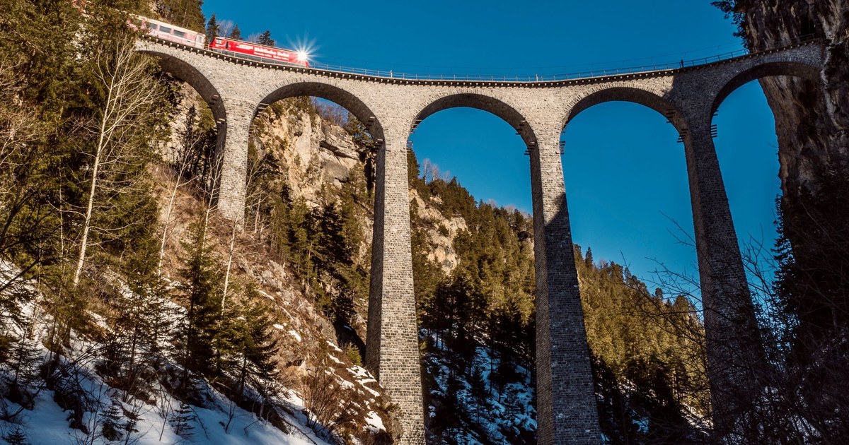 Red train crossing the curved stone Landwasser Viaduct near Filisur in the snowy Swiss Alps